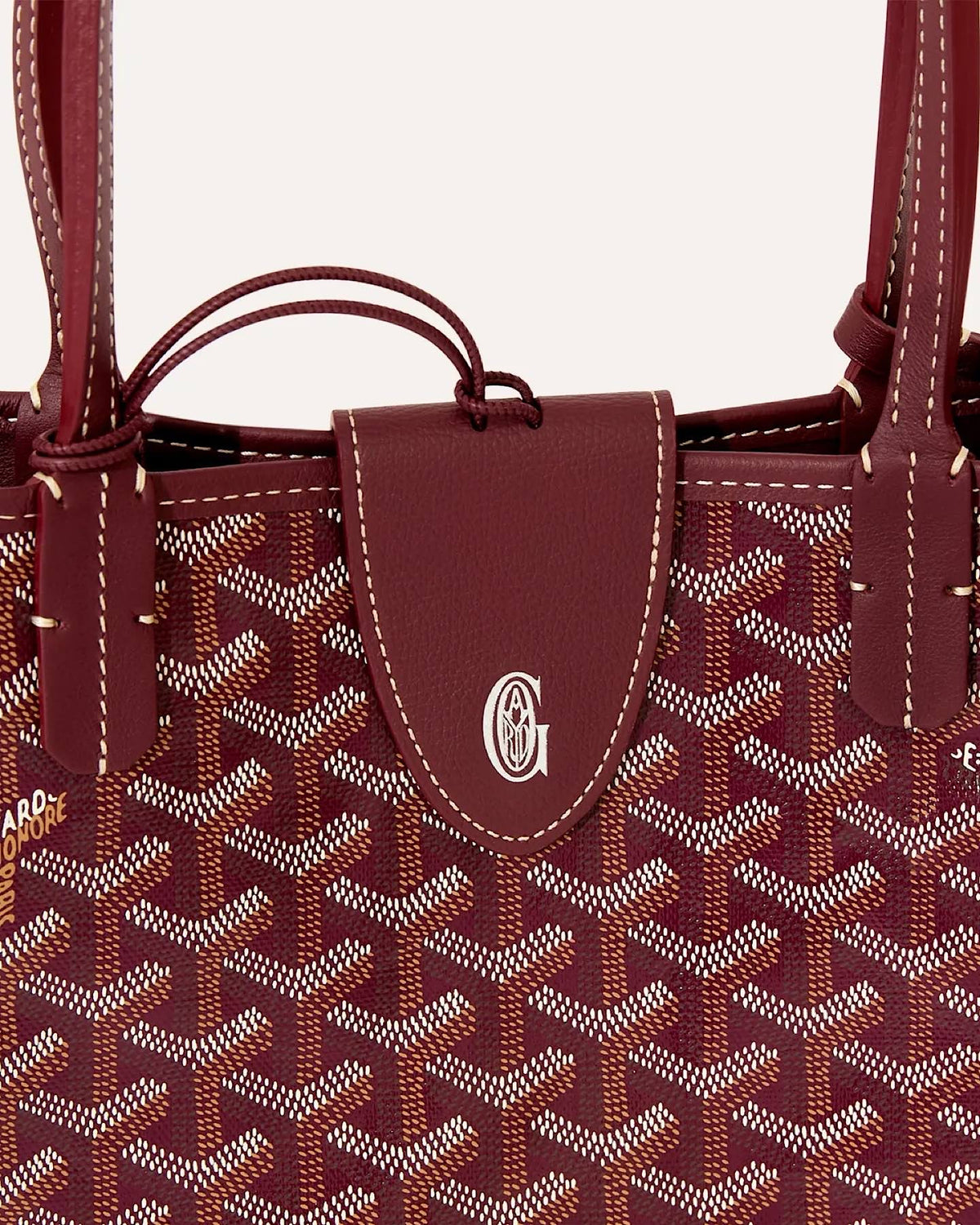 Close-up of Goyard Sac Anjou Mini featuring burgundy Goyardine canvas, leather trim and signature front tab detail.